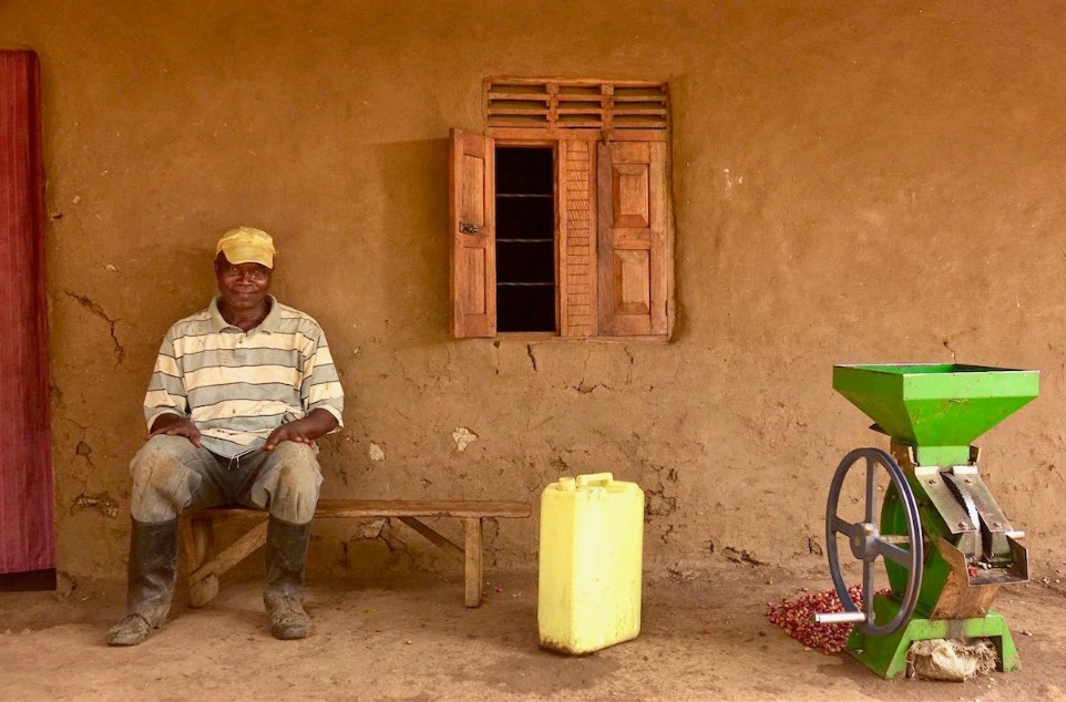 One African Coffee farmer smiling sitting beside a depulping machine 